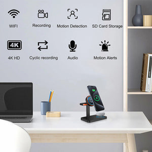 A Universal Charger SpyCam on a wireless charging stand rests on an office desk, featuring WiFi, recording, motion detection, SD card storage, 4K HD, cyclic recording, audio capabilities, and motion alerts—disguised cleverly as a regular smartphone charger.