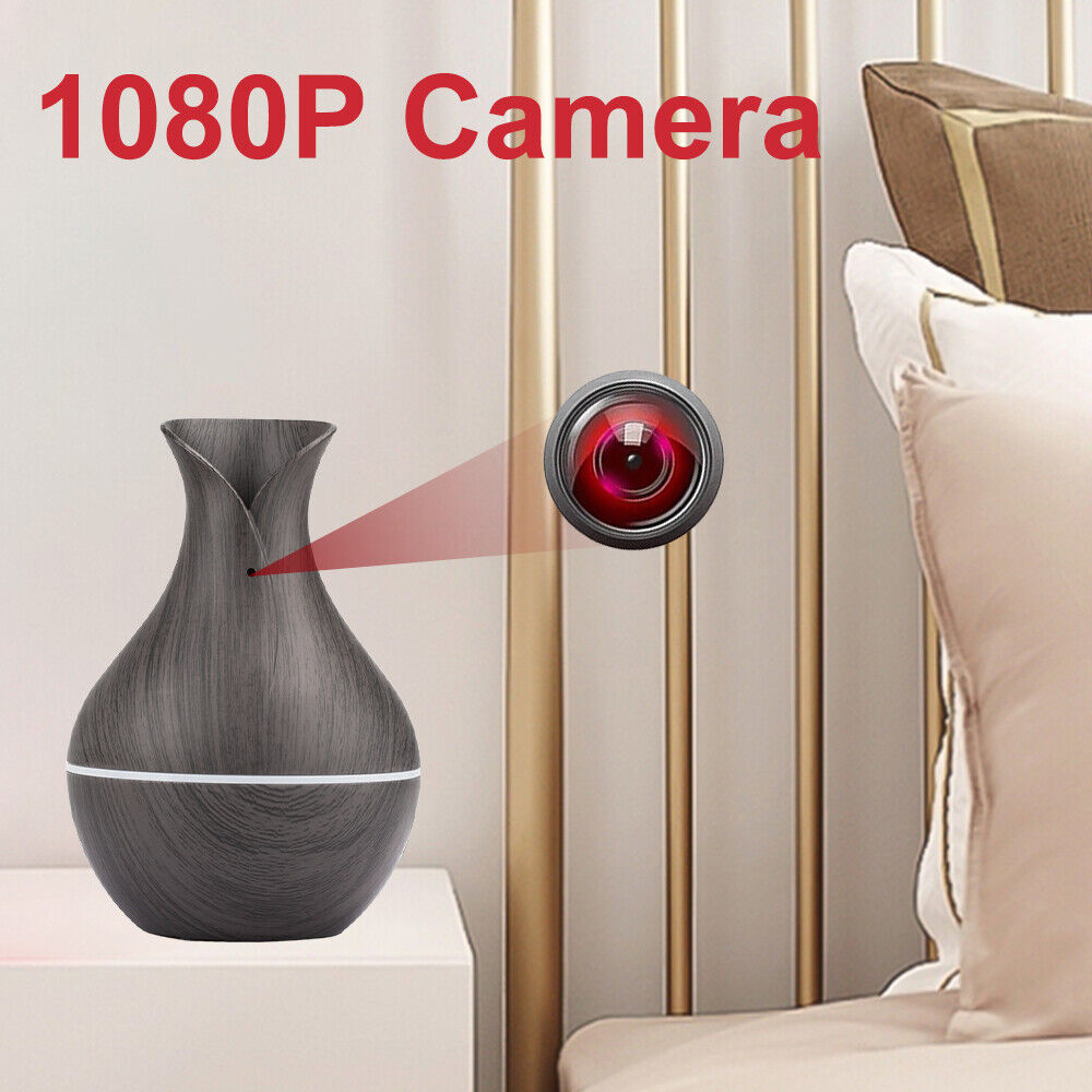 A Black Decorative Display SpyCam acts as a discreet vase with a dark wood pattern, effortlessly blending into modern decor when placed on a bedside table next to a gold metal bed frame and white pillows.