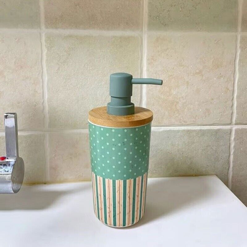 A Cute Decorative Display SpyCam, styled as a green and beige soap dispenser with polka dots and stripes, sits on a white bathroom counter against beige tiled walls.