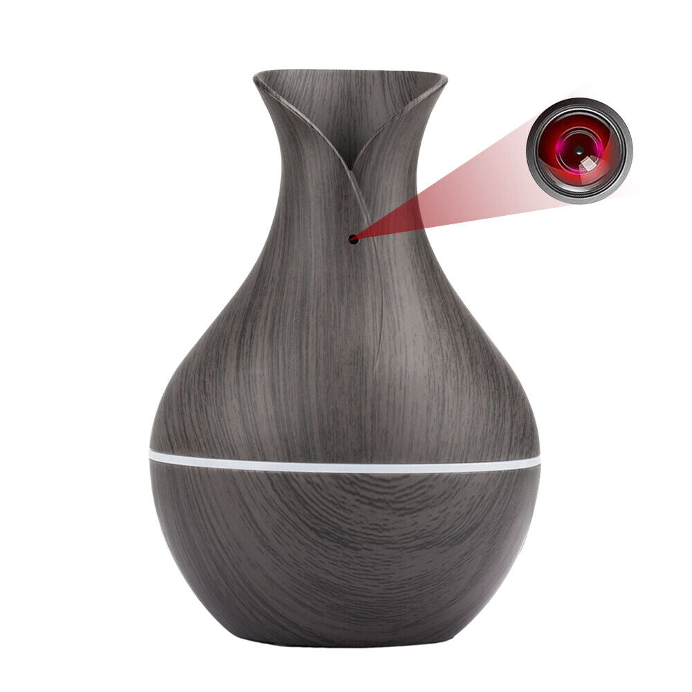 The Black Decorative Display SpyCam is a gray vase-shaped object with a wood texture, discreetly hiding a camera behind its lens at the top front, marked by a subtle red beam. It effortlessly integrates into home décor while featuring advanced espionage technology.
