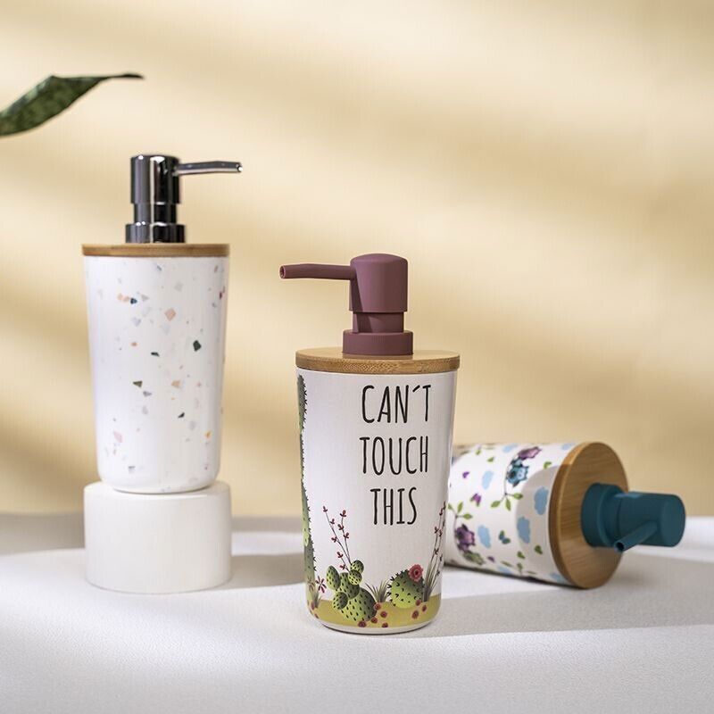 Three soap dispensers rest on a white surface, two upright and one lying down. The center dispenser features playful text and a plant design, disguising the Cute Decorative Display SpyCam with 1080P recording. A softly lit background enhances the scene's charm.