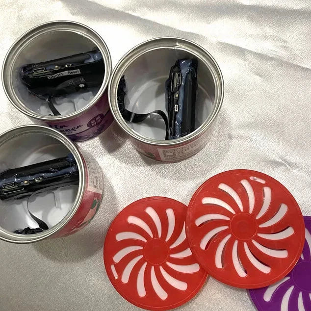 Two Fake Decorative Display SpyCams, cleverly disguised as open cans, are revealed on a white surface with red and pink spiral-patterned covers placed next to them.