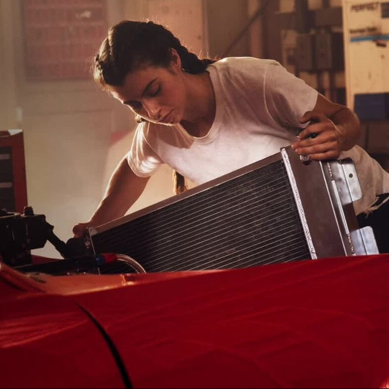 A person in a white shirt installs a substantial car component under the vehicle's hood in the garage, ensuring seamless integration with the Tire Pressure & Temperature Monitoring System to enhance driving safety.