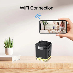 A smart speaker sits on a table with a book and plant, connected via WiFi. Nearby, a phone displays a living room scene with two people and the speaker. The discreetly placed Universal Charger Night Light SpyCam ensures added security.