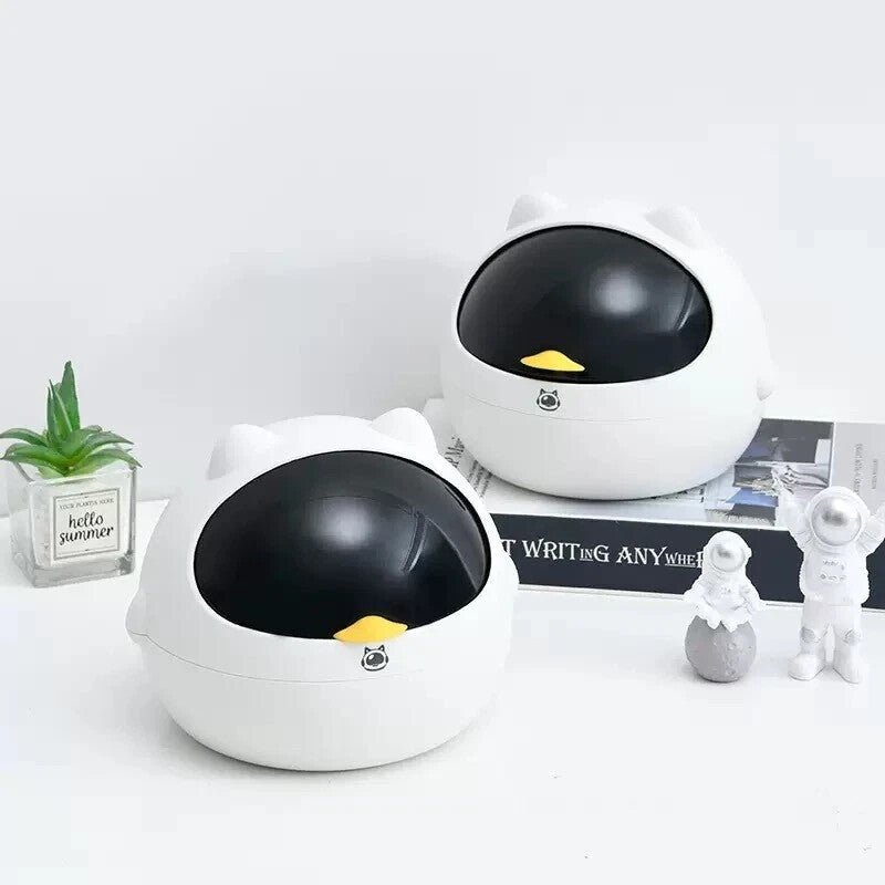 Two Cute Display SpyCam cameras, round and white with black domes and yellow beaks, sit on a table near books, a potted plant, and figurines—perfect for discreet home surveillance.