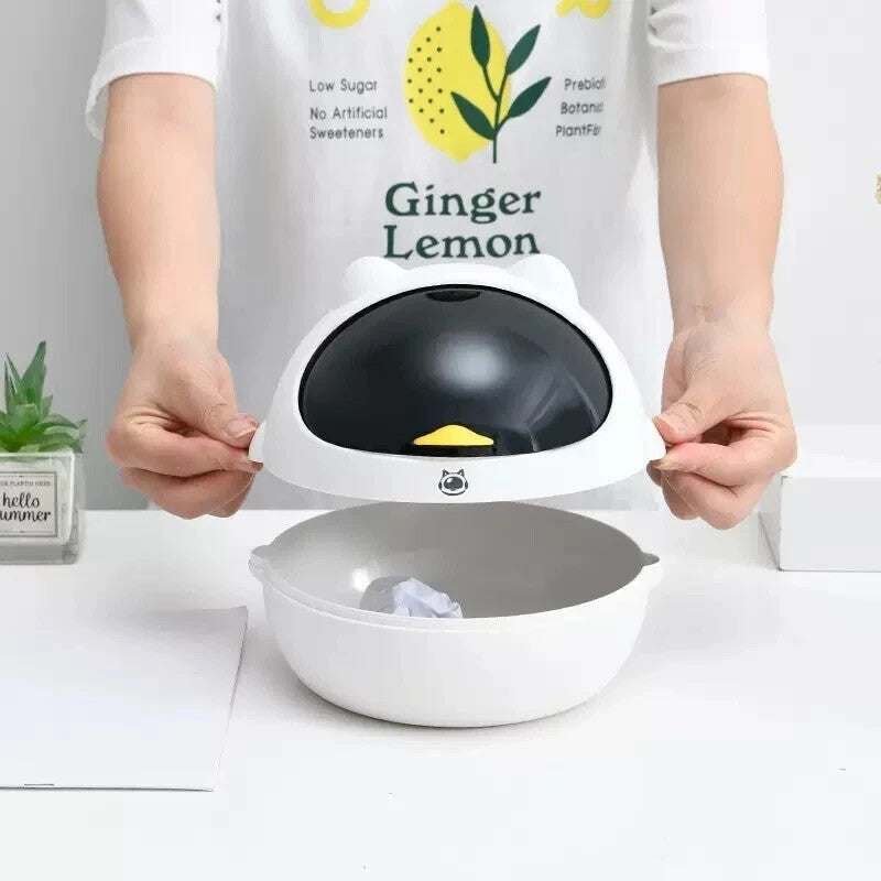 A person opens a Cute Display SpyCam, a small white tabletop trash bin with a black lid and yellow handle; inside is crumpled paper—ideal for discreet home surveillance.