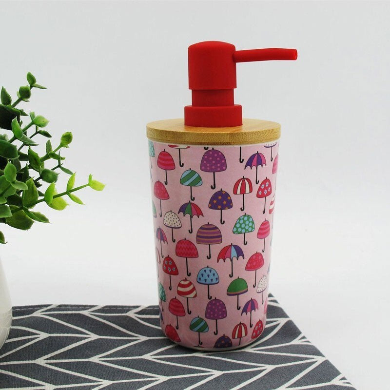 The Cute Decorative Display SpyCam discreetly blends in, cleverly designed as a soap dispenser with a red pump and wooden lid, showcasing colorful umbrellas on a pink background. It records video in 1080P resolution. A green plant is partially visible on the left.