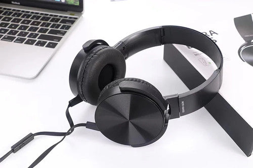 Wired Bass Headphone in black, featuring an attached microphone and ergonomic over-ear design, is displayed on a white surface beside a laptop and product packaging.