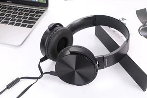 Wired Bass Headphone in black, featuring an attached microphone and ergonomic over-ear design, is displayed on a white surface beside a laptop and product packaging.