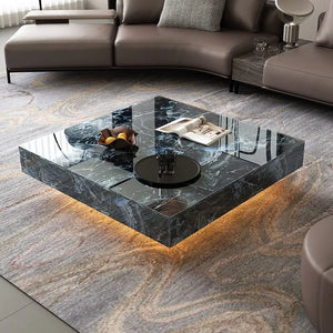 A modern living room showcases the Modern Luxe Coffee Table with a glossy black marble finish, underlighting, fruit bowl, and magazine, surrounded by beige sofas on a textured rug—ideal for chic contemporary interiors.