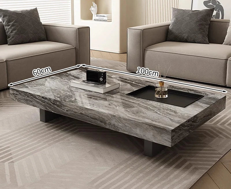 The Modern Luxe Coffee Table, a rectangular marble piece measuring 100 x 60 cm, sits between two beige sofas on a patterned rug—an elegant addition to any modern interior.