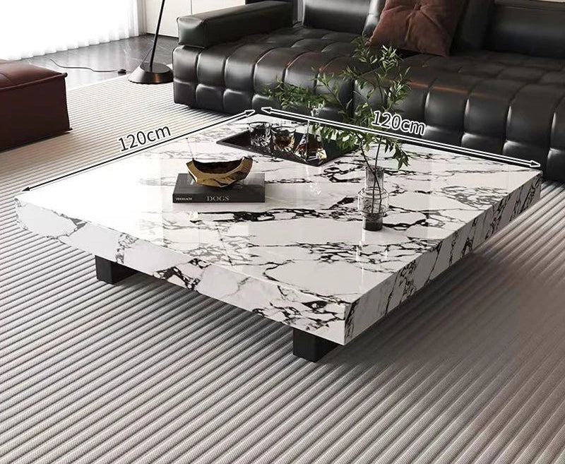 The Modern Luxe Coffee Table, a square marble minimalist piece with black legs (120cm x 120cm), sits atop a striped rug beside a black sofa—ideal for stylish modern living rooms.