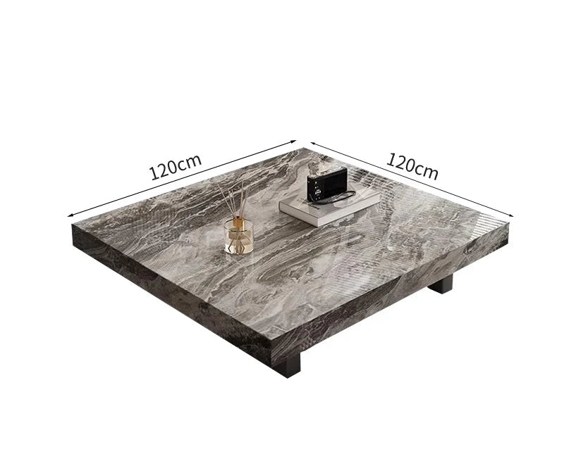 The Modern Luxe Coffee Table features a square marble top (120x120 cm) with four short legs. Ideal for modern interiors, it's styled with a tray, books, and a reed diffuser arranged on the surface.