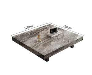The Modern Luxe Coffee Table features a square marble top (120x120 cm) with four short legs. Ideal for modern interiors, it's styled with a tray, books, and a reed diffuser arranged on the surface.