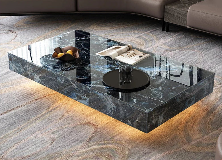 The Modern Luxe Coffee Table features a rectangular black marble top with underlighting and a glossy finish, displayed with fruit, a magazine, and a glass on a patterned rug—ideal for elevating modern interiors.