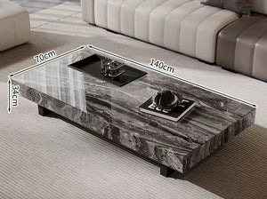 The Modern Luxe Coffee Table features a rectangular marble top with black and gray veining, measuring 140×70×34 cm. Perfect for modern interiors, it looks stunning on a light rug and can be styled with decor items.