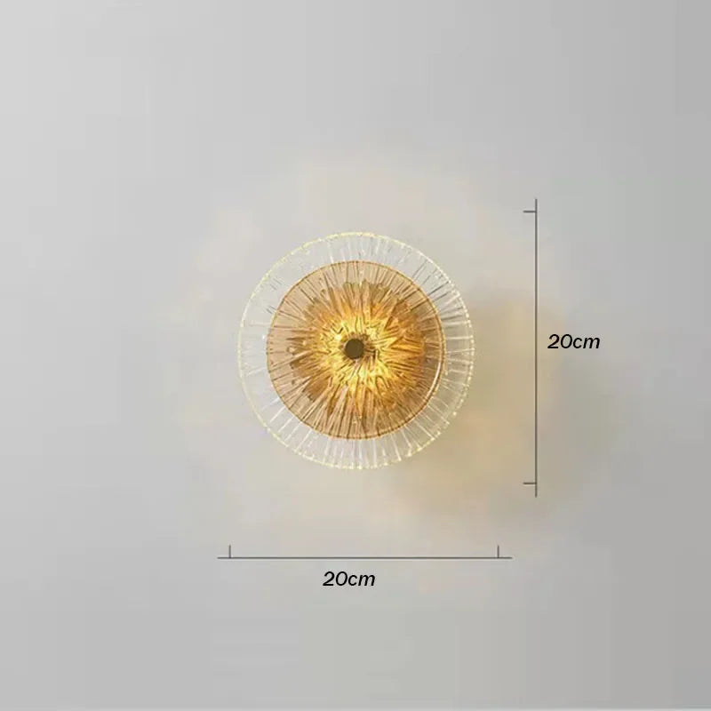 The Amber Deco Wall Sconce is a round, nature-inspired light measuring 20cm by 20cm, shown glowing elegantly against a simple grey background.