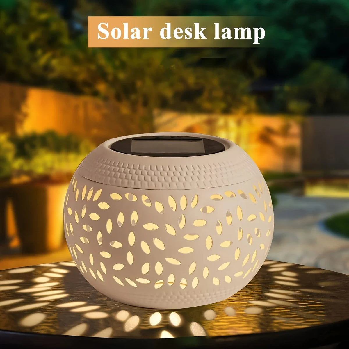 Round, white hollow iron lamp with a cutout leaf pattern, glowing on a table outdoors at dusk. Text reads “Solar Orb Lamp” at the top.