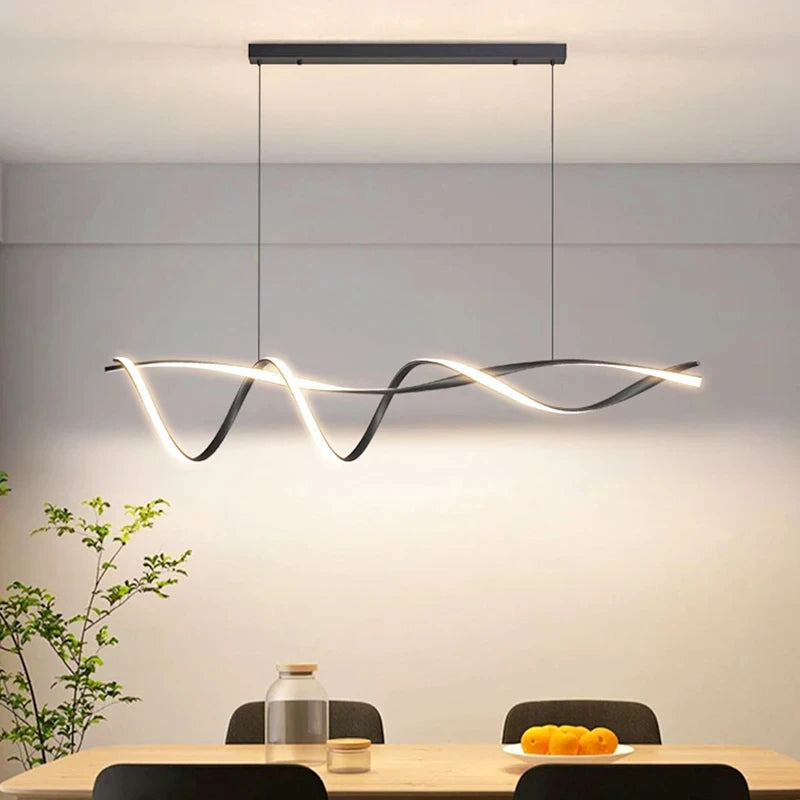 The sculptural Stylish Pendant Light elegantly hangs over a dining table, with a fruit bowl, jar, and plant below, epitomizing minimalist design in this modern setting.