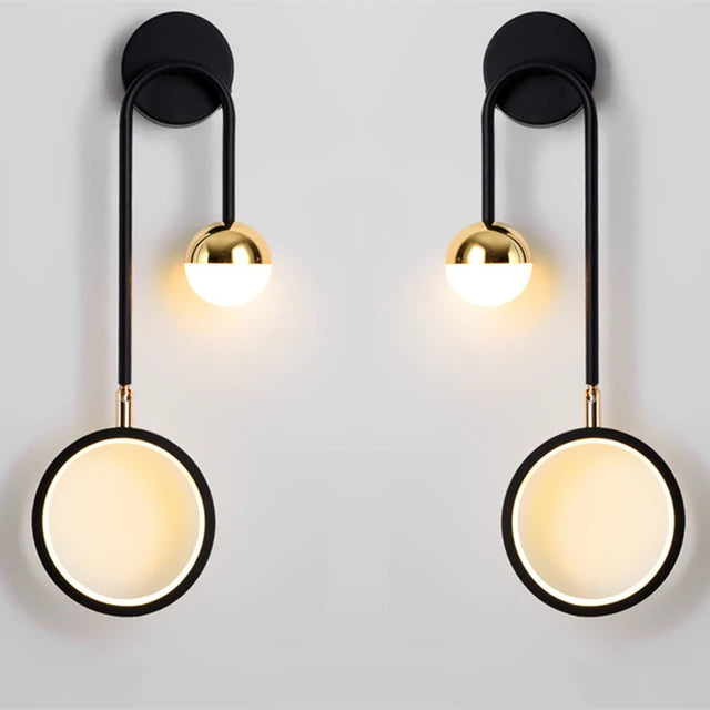 Featuring two modern Hanging Circle Wall Lights, one with black metal arms and a circular light, and the other with a gold sphere light, mounted on a white wall, these fixtures embody stylish Nordic design elements.