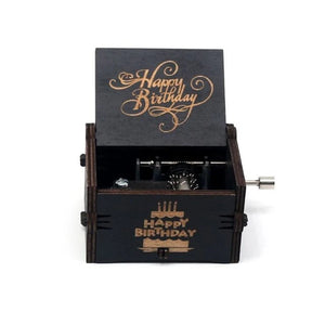 The Happy Birthday Music Box is a small wooden music box with an open lid that displays the words "Happy Birthday." The front of the box also features "Happy Birthday" text. It has a metal crank handle on the side, making it a perfect birthday gift.