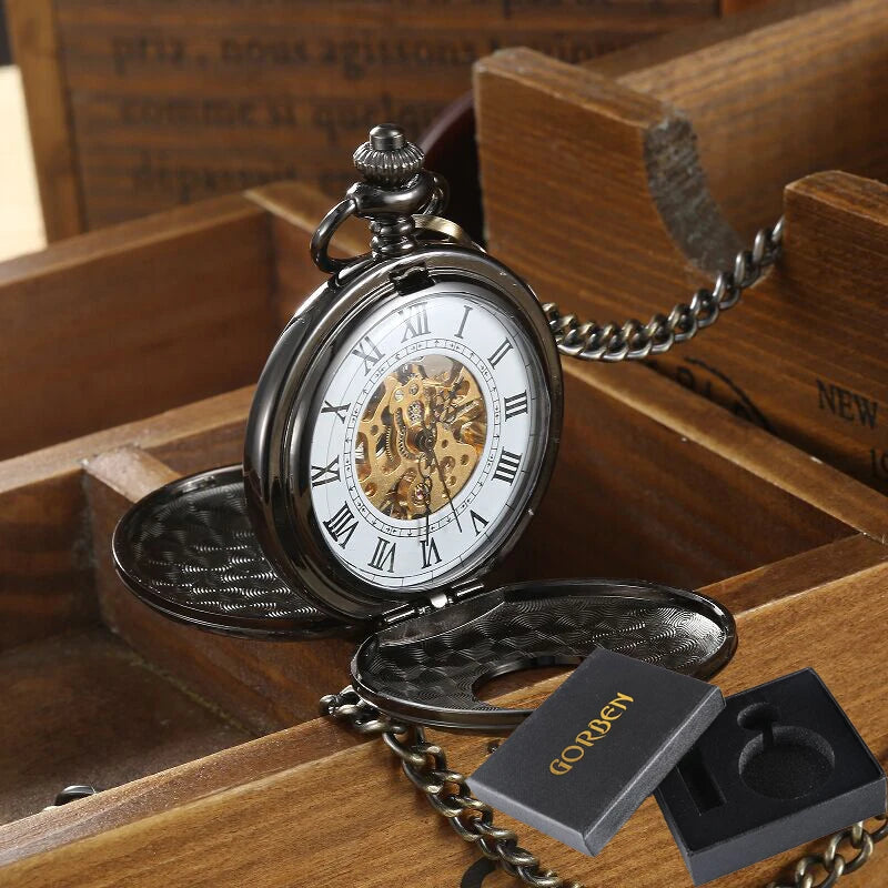 The Vintage Mechanical Pocket Watch, featuring visible gears and Roman numerals, rests in a wooden box with a black "GORBEN" branded watch box beside it.