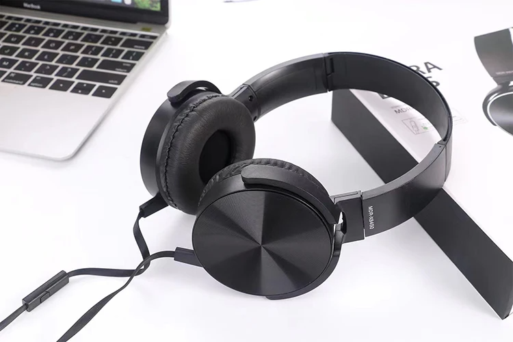 The Wired Bass Headphone, a black over-ear model with cushioned headband and ear pads for ergonomic comfort, is shown on a white desk beside a laptop and product packaging.