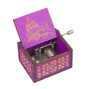 Introducing the Happy Birthday Music Box: a vibrant purple and gold, hand-cranked music box featuring a winding handle and an open lid that beautifully displays a birthday cake alongside the words "Happy Birthday.