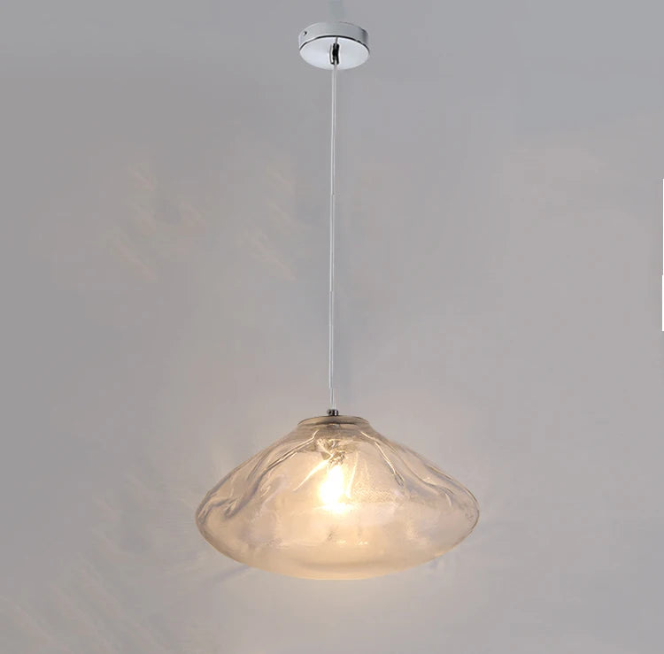 The Luxe Cloud Glass Pendant Light features a translucent, uniquely shaped glass shade suspended from a white ceiling by a slim cord, casting elegant illumination below.