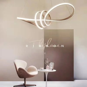 A modern room featuring a Stylish Pendant Light exuding sculptural quality, accompanied by a sleek white chair and a small round table adorned with a plant and framed photo.