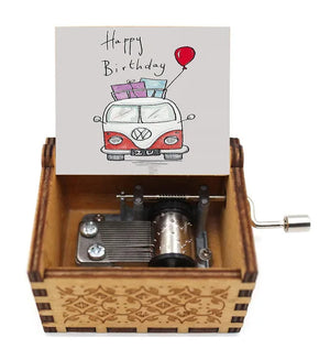 The "Happy Birthday Music Box" features a hand-cranked mechanism enclosed within an engraved border. When opened, the lid reveals a charming drawing of a red van with gifts on top and a cheerful "Happy Birthday" message.