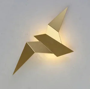 The Modern Flying Bird Wall Sconce is a minimalist, gold-colored wall lamp featuring an abstract geometric design that softly illuminates from behind.