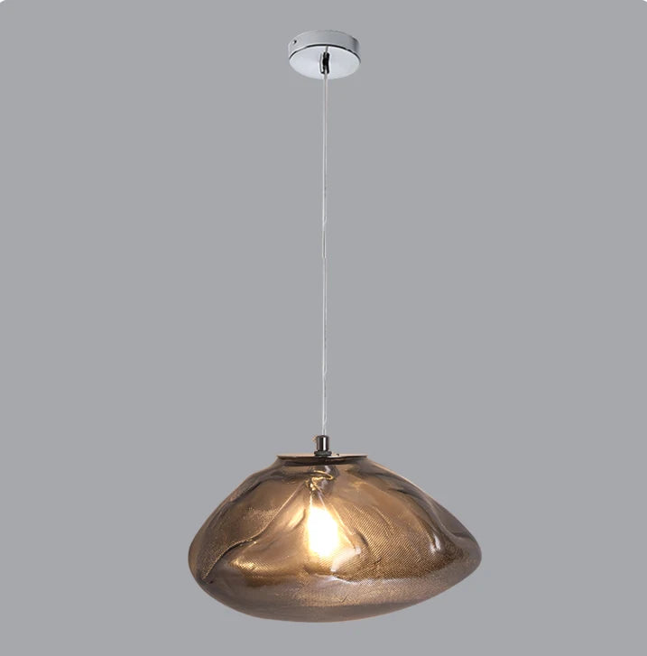 The Luxe Cloud Glass Pendant Light features a sculptural design with a translucent smoked glass shade and visible bulb, suspended from the ceiling by a cord against a plain grey background.