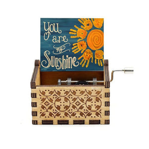 A "Music Box - You Are My Sunshine" crafted from wood, featuring a hand-crank rotary handle and an open lid displaying a sign that reads "You Are My Sunshine," accompanied by a sun drawing.