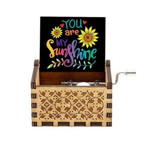 The Music Box - You Are My Sunshine features a romantic rotary handle and intricate carvings. Open the lid to reveal the message "You Are My Sunshine" in colorful text, accompanied by charming sunflower illustrations, all operated by a hand crank.