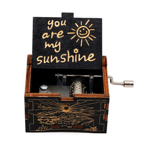 The Music Box - You Are My Sunshine is a romantic wooden piece with a rotary handle, showcasing an open lid adorned with the text "You Are My Sunshine" and a sun illustration, along with intricate carvings on its exterior.