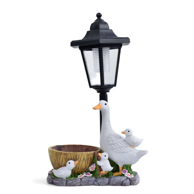 Enhance your cottage garden with the charming Solar Goose Lamp, showcasing a mother goose, three playful goslings, a small bowl, and vibrant flowers at the base—an enchanting piece of decorative garden lighting for any outdoor space.