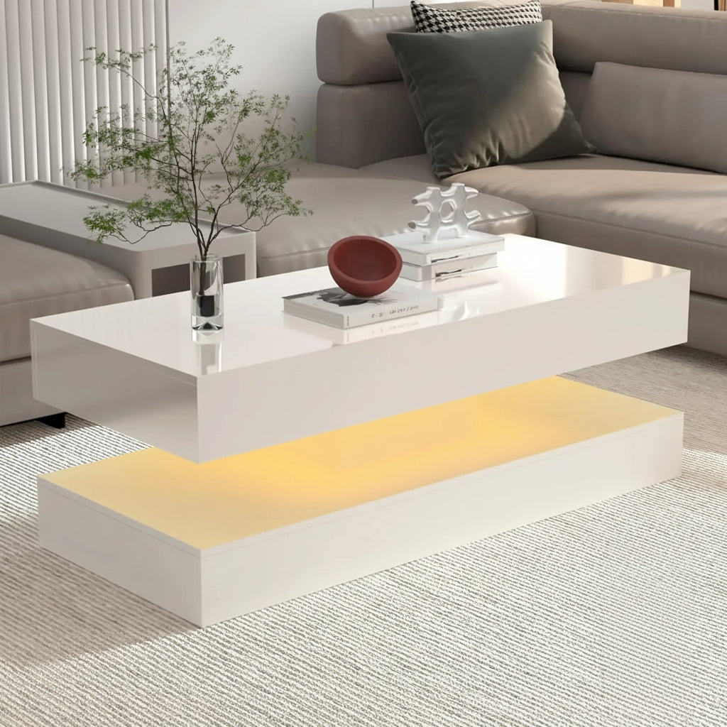 The Premium Coffee Table, a modern white design with a floating top and ambient yellow LED lighting, is placed in front of a beige sectional sofa and displays decorative items on its surface.