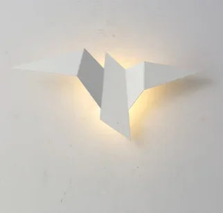 A minimalistic, nature-inspired wall-mounted light fixture resembling an origami bird, the Modern Flying Bird Wall Sconce illuminates a soft light against a plain white background.