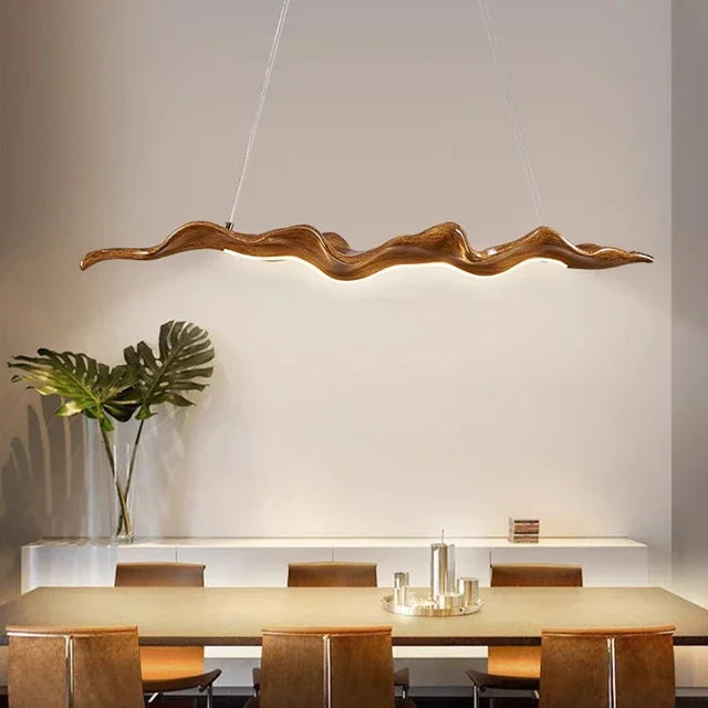 Modern dining room with an organic touch featuring a Leaf Pendant Light above a rectangular table, complemented by brown chairs, a large leafy plant, and minimalist decor.