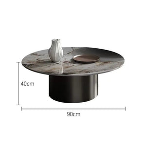 The Premium Round Coffee Table features a marble top, black cylindrical base, and comes accented with a vase and tray. Dimensions: 90 cm wide, 40 cm high.