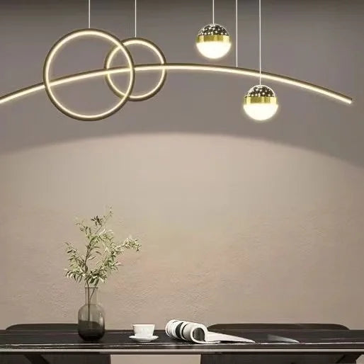 The Stellar Pendant Light, with its circular geometric design, elegantly illuminates a wooden table adorned with a vase, open book, and white cup.