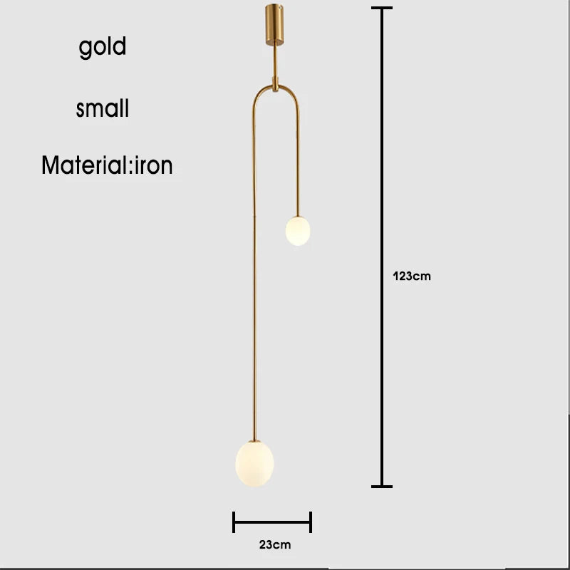 The Minimalist Line Light is a gold pendant fixture with a sculptural design featuring two spherical bulbs at each end. Measuring 123 cm in height and 23 cm in width, it's crafted from iron and boasts a modern lighting aesthetic coupled with a minimal mounting system for effortless elegance.