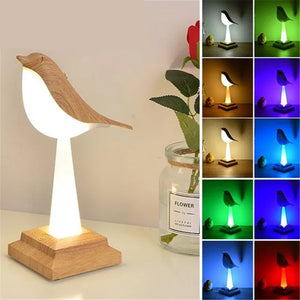 A Bird Table Night Light with a minimalist design sits on a wooden base, casting a warm glow next to a jar with a red rose. Multiple images on the right showcase the night light in various colors—white, yellow, orange, pink, red, blue, and green.