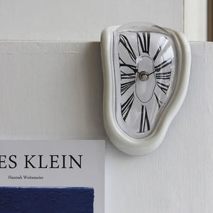 A Salvador Dali-inspired clock hanging on a wall next to a book, adding an artistic flair to the space.
