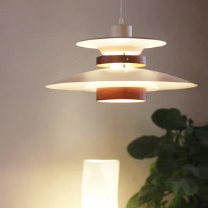 A pendant light with a natural wood finish hanging over a Scandinavian-styled table with a plant on it.