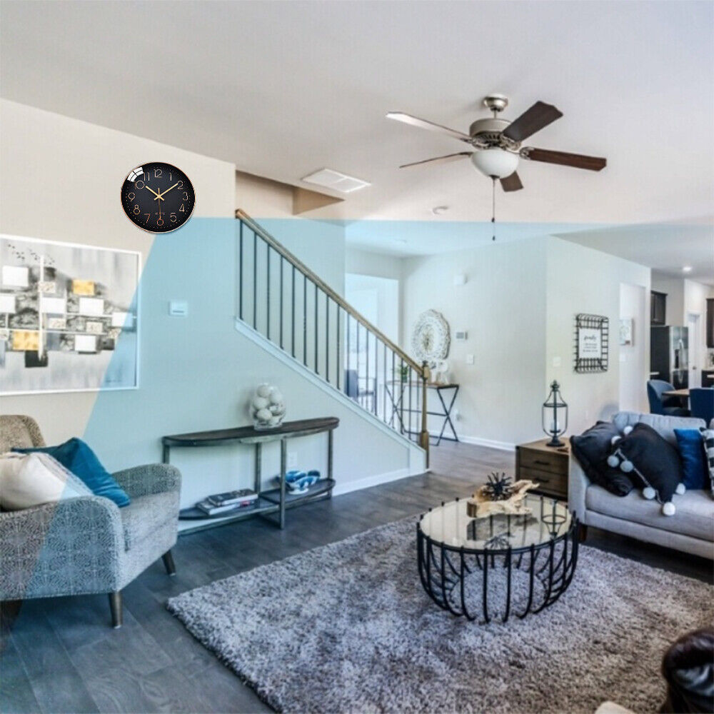 A modern living room features a grey armchair, dark rug, glass coffee table, wall art, and ceiling fan. A staircase with a grey bannister leads to the upper level. For added security, an analog wall clock equipped with the Wall Clock SpyCam ensures discreet motion detection.

