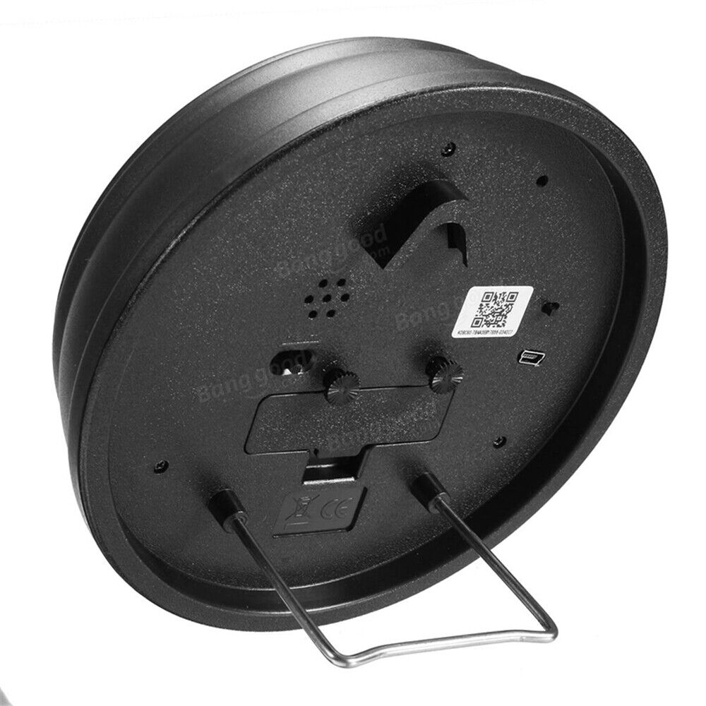 The Bird Clock SpyCam is a black circular metallic device with a handle, QR code, embossed brand name, two connectors, and adjustable knobs underneath. It includes motion detection for enhanced surveillance functionality.