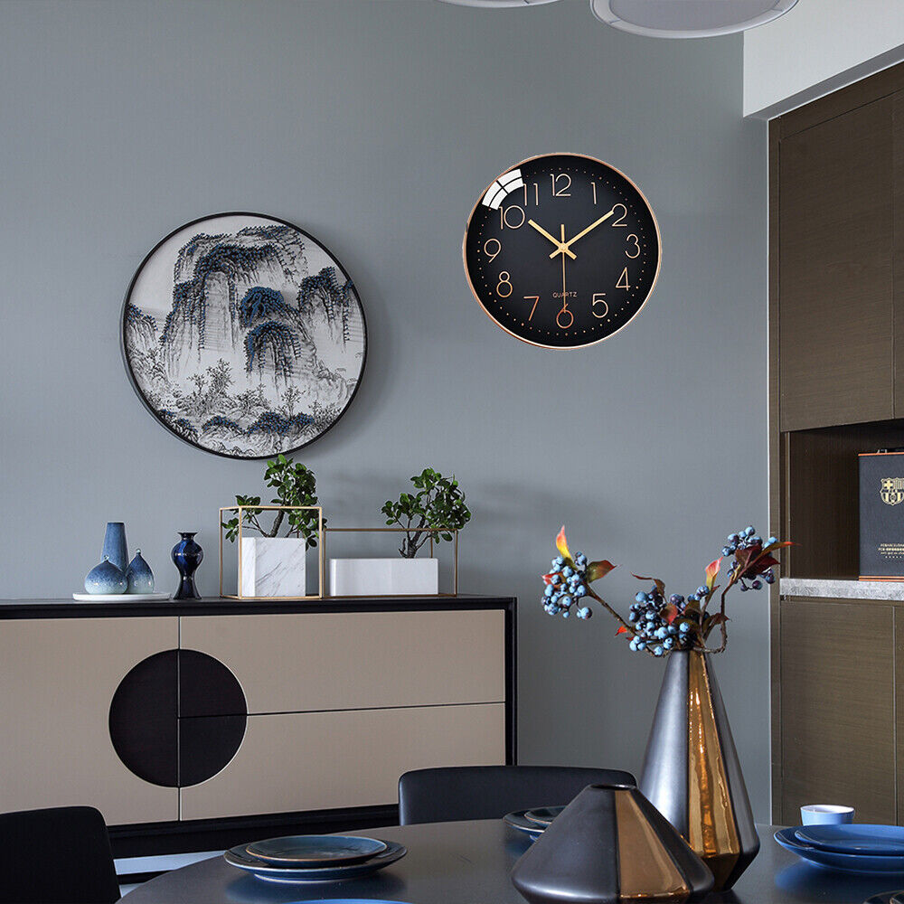 A modern dining room features a round black wall clock, specifically the Wall Clock SpyCam with motion detection, and a landscape painting on a gray wall. A sideboard displays vases, while the table is set with blue dinnerware and a metallic vase with flowers. The room feels high-tech yet cozy.