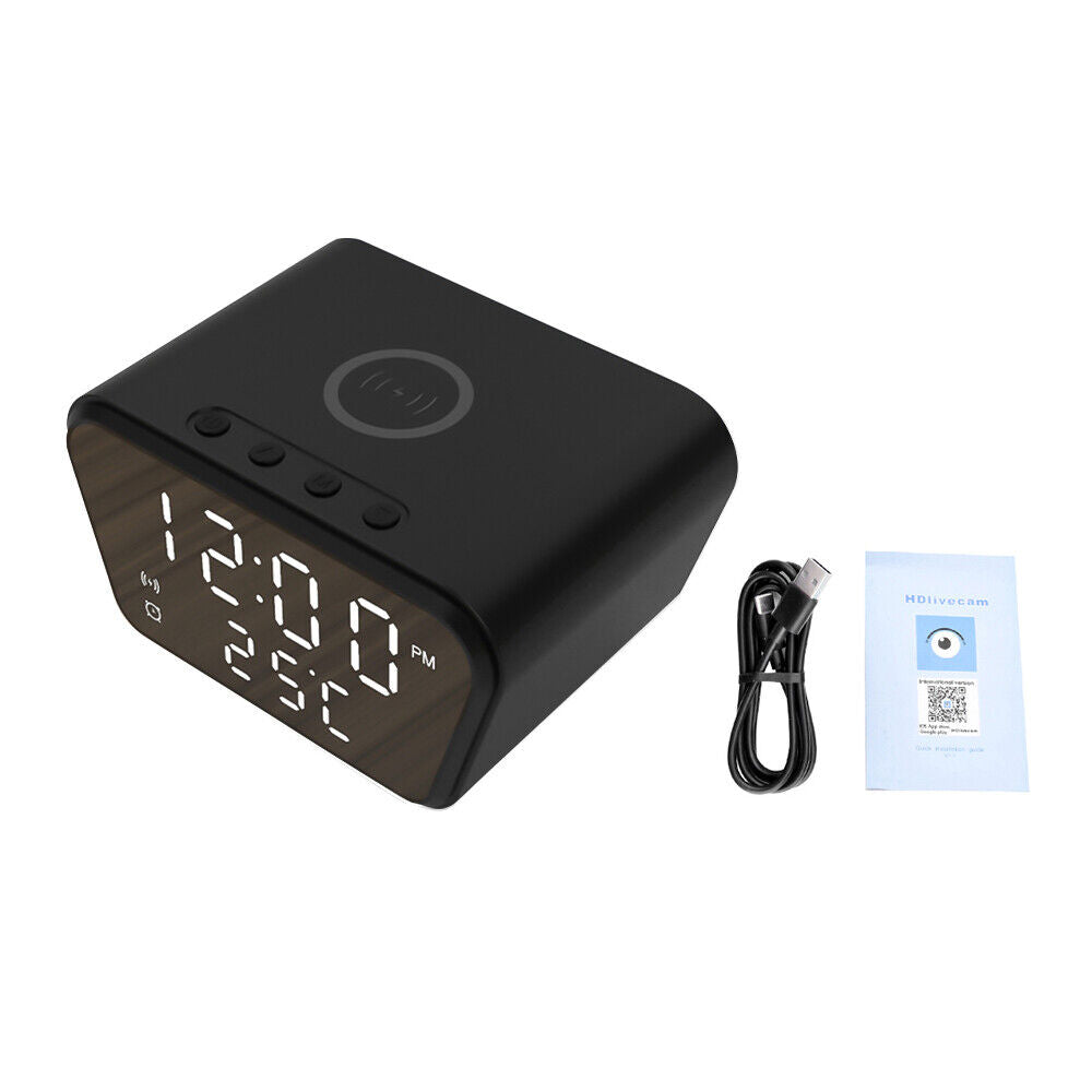 The Clock Charger SpyCam is a sleek black digital clock displaying 12:00 and 23°C, with top buttons. It comes with a USB cable and "HDlivecam" manual, ideal for discreet home surveillance.
